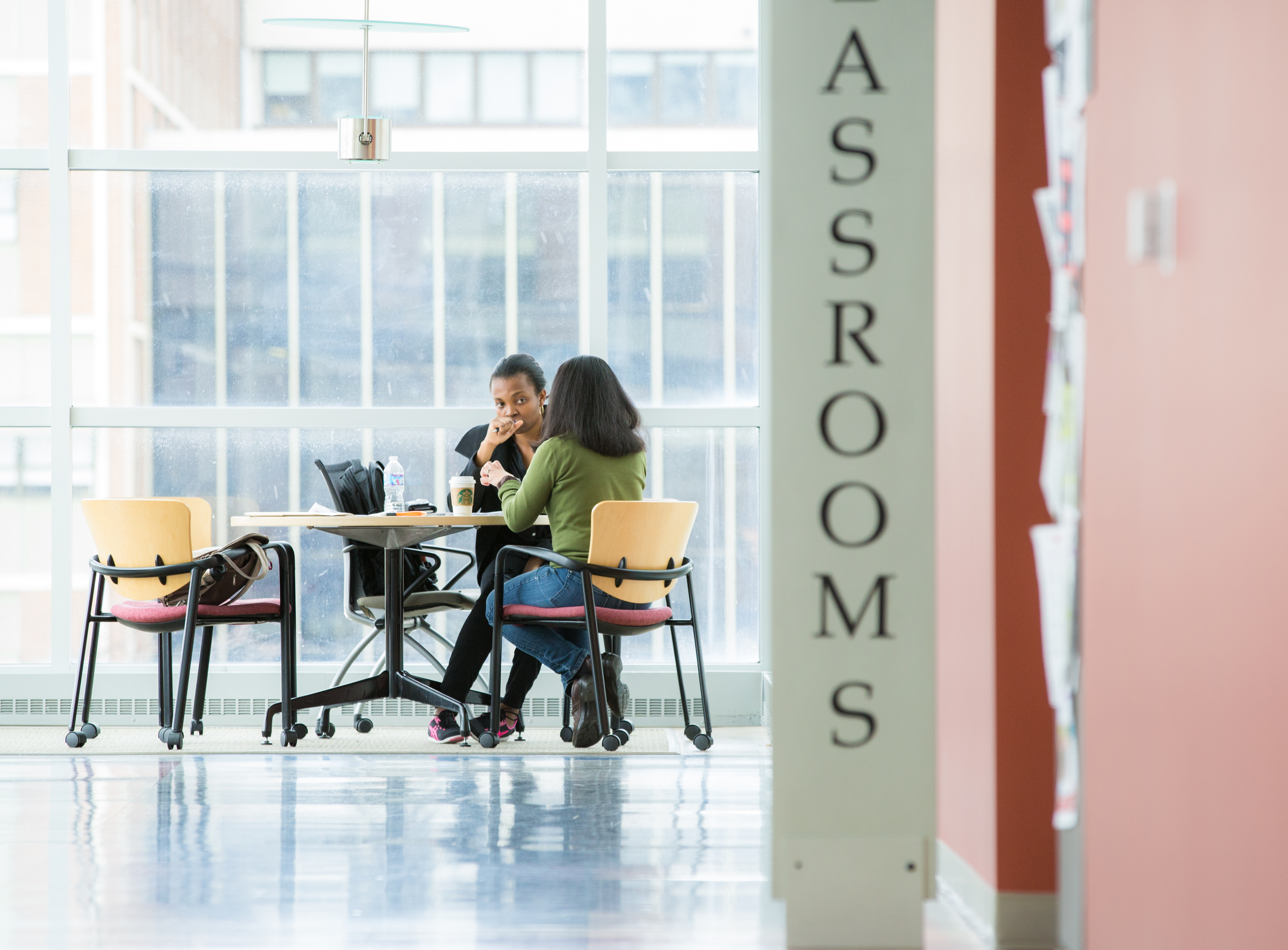 2 students sitting in a lobby outside of classrooms