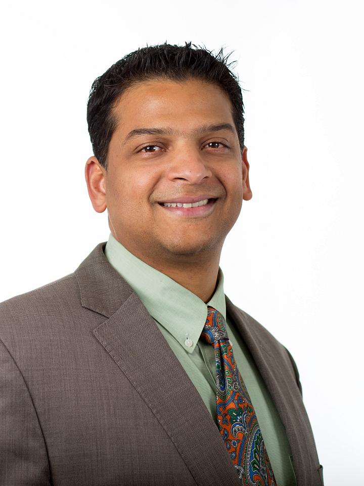 Dr. Venkata Kashyap Yellepeddi in portrait photo with grey suit, green shirt, and orange and blue tie